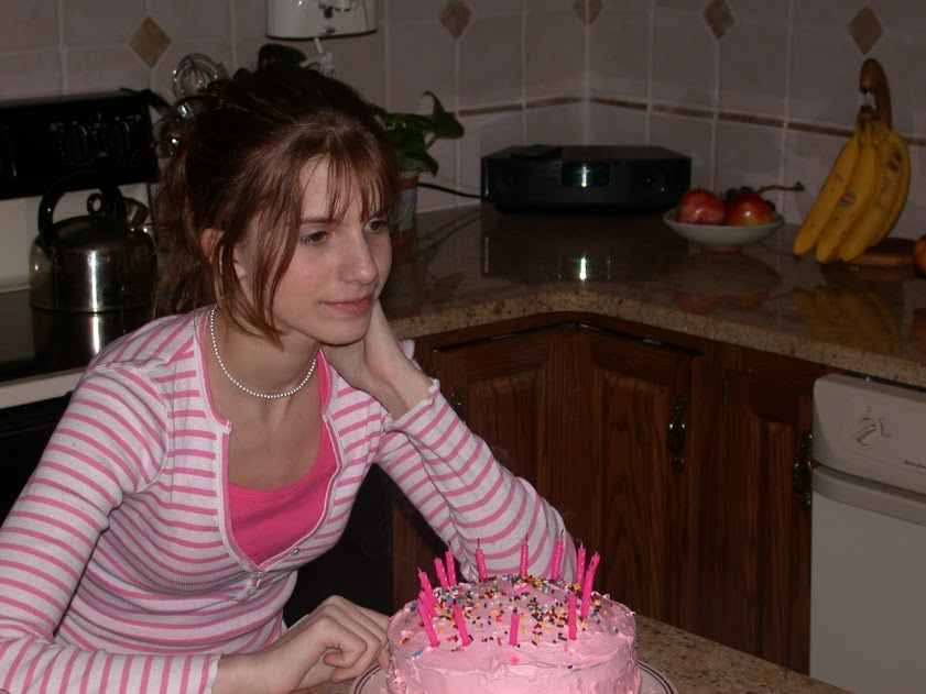 A woman in a pink striped shirt sits in front of a pink birthday cake