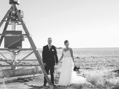 A black and white photo of a bride and groom holding hands in a field.