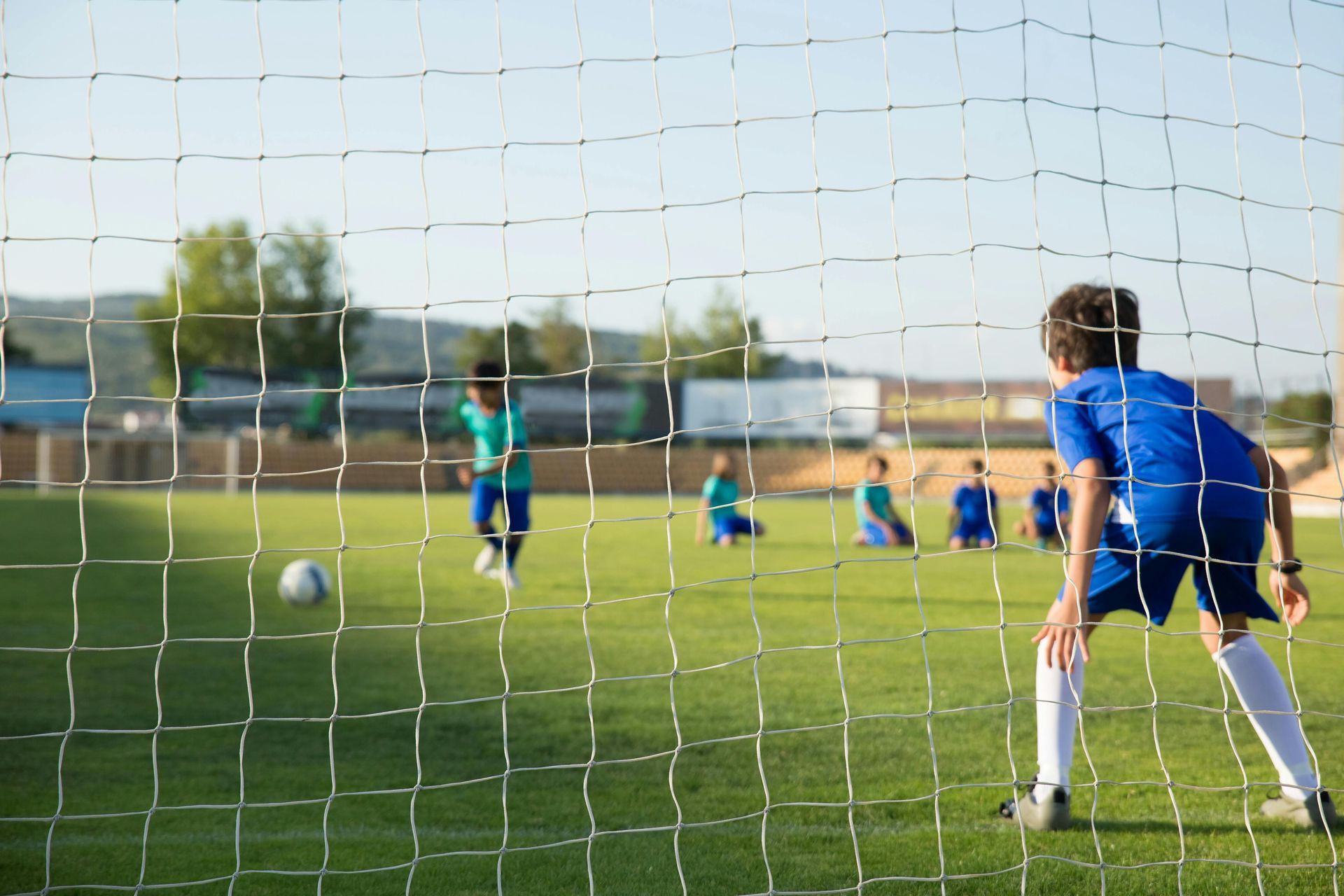 Young boy standing in net as goalie getting ready to block soccer ball kick from other team.
