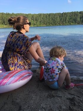A woman and a child are sitting on the beach looking at the water.
