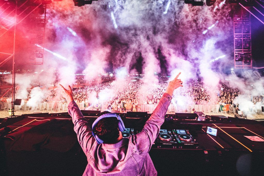 A dj is playing music at a concert with his arms in the air.