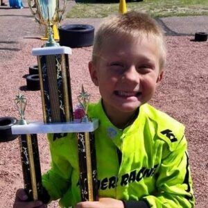 A young boy in a yellow jacket is holding a trophy