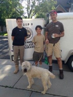 Three men and a boy are standing next to a dog in front of a trailer.