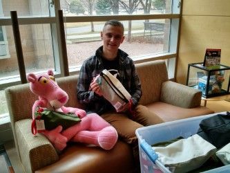 A man is sitting on a couch holding a pink panther stuffed animal.