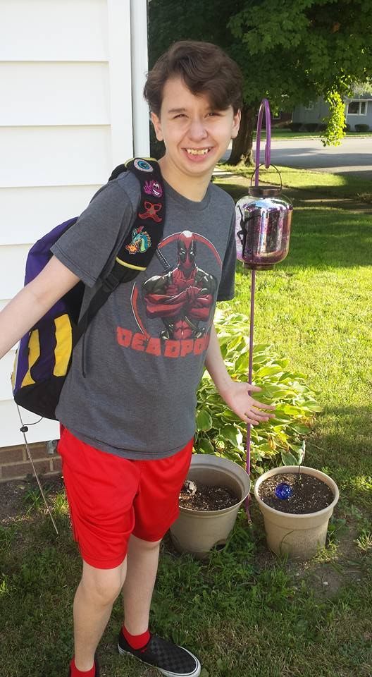 A young boy wearing a gray shirt and red shorts is standing in front of a house.