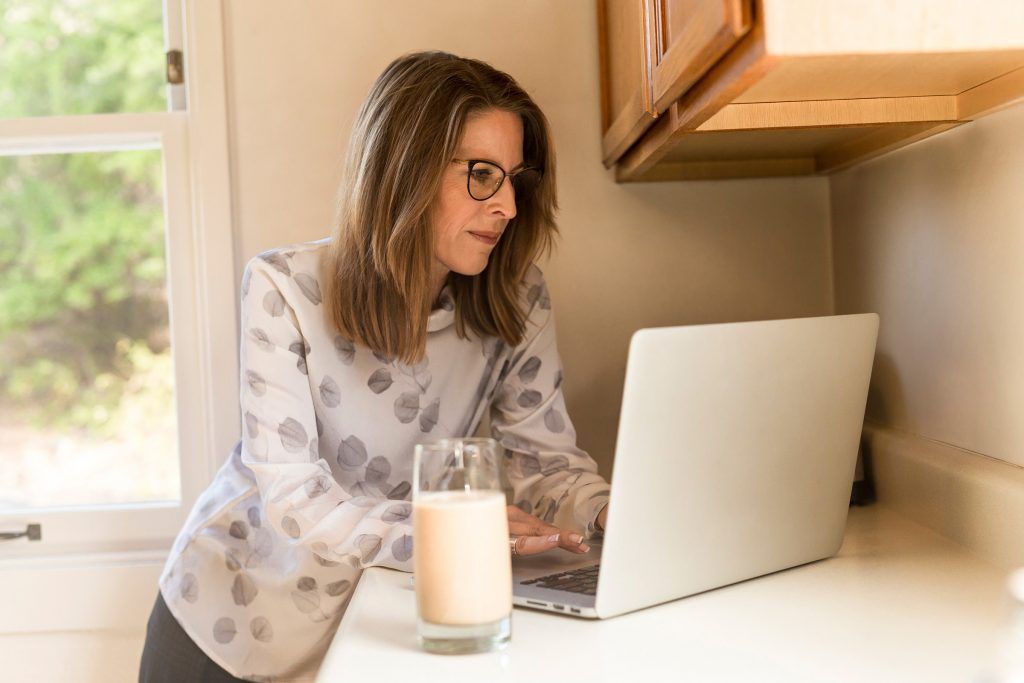 A woman is drinking milk while using a laptop computer.