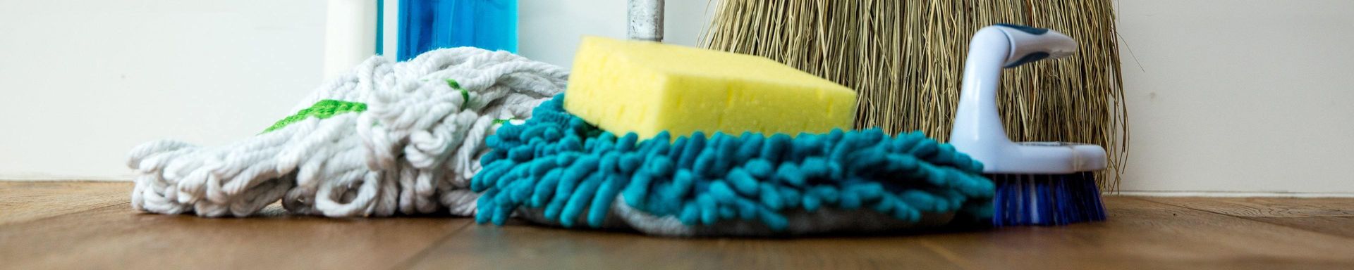 A mop , sponge , and brush are sitting on a wooden floor.