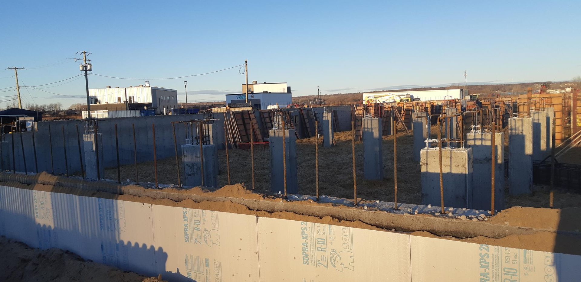 Chantier de construction avec fondations et colonnes en béton, ciel bleu en arrière-plan.