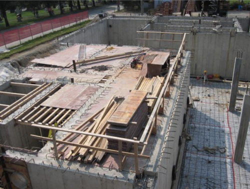 Chantier de construction avec murs de fondation en béton, coffrage en bois et armatures apparentes.