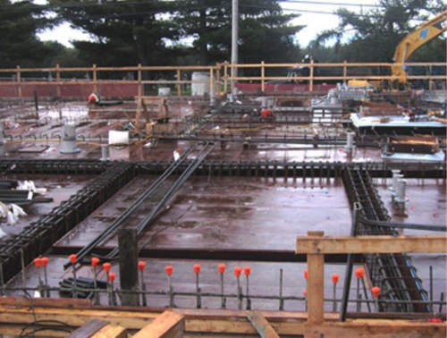 Chantier de construction avec armature en acier ; capuchons de sécurité orange ; coffrages en bois.