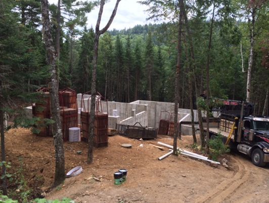 Chantier : Fondations en béton entourées d'arbres ; présence de matériaux et d'un camion.