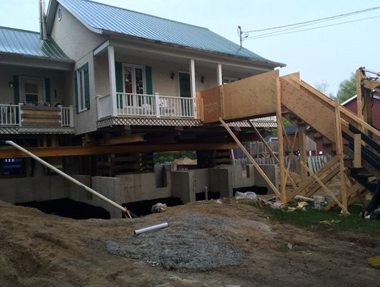 Maison surélevée sur des supports en bois pendant les travaux de fondation ; escalier temporaire.