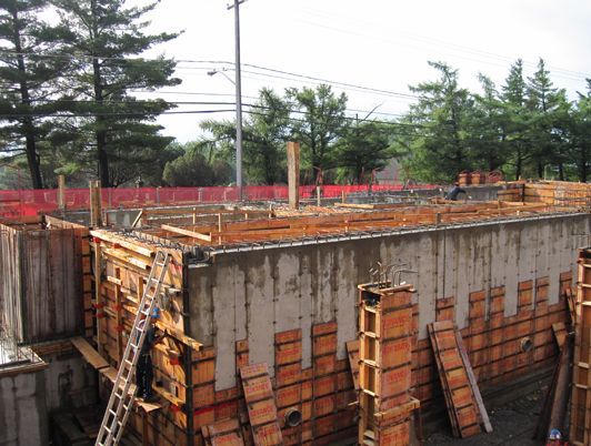 Chantier de construction avec coffrages en béton, supports en bois et clôture de sécurité rouge.