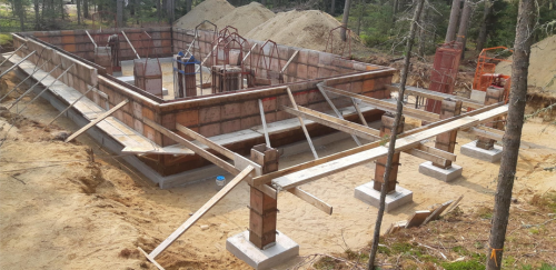 Chantier de construction avec fondations en briques, supports en bois et sable.