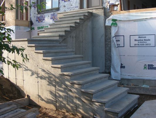 Escalier extérieur en béton menant à l'étage ; bâtiment inachevé en arrière-plan.