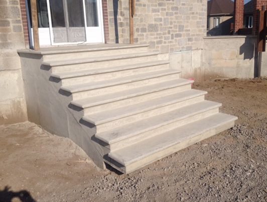 Escaliers en béton menant à une porte ; chantier inachevé ; couleurs beige et grise.