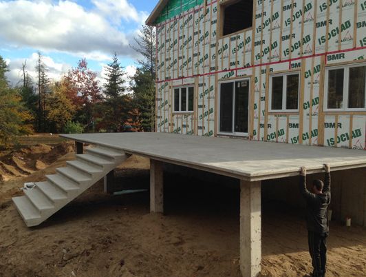 Terrasse en béton avec escalier attenant à une maison en construction. Une personne se trouve près du bord de la terrasse.