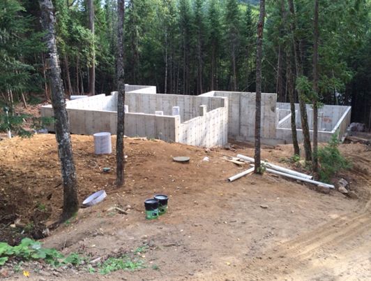 Fondations en béton d'un bâtiment en construction, entourées de terre et d'arbres.
