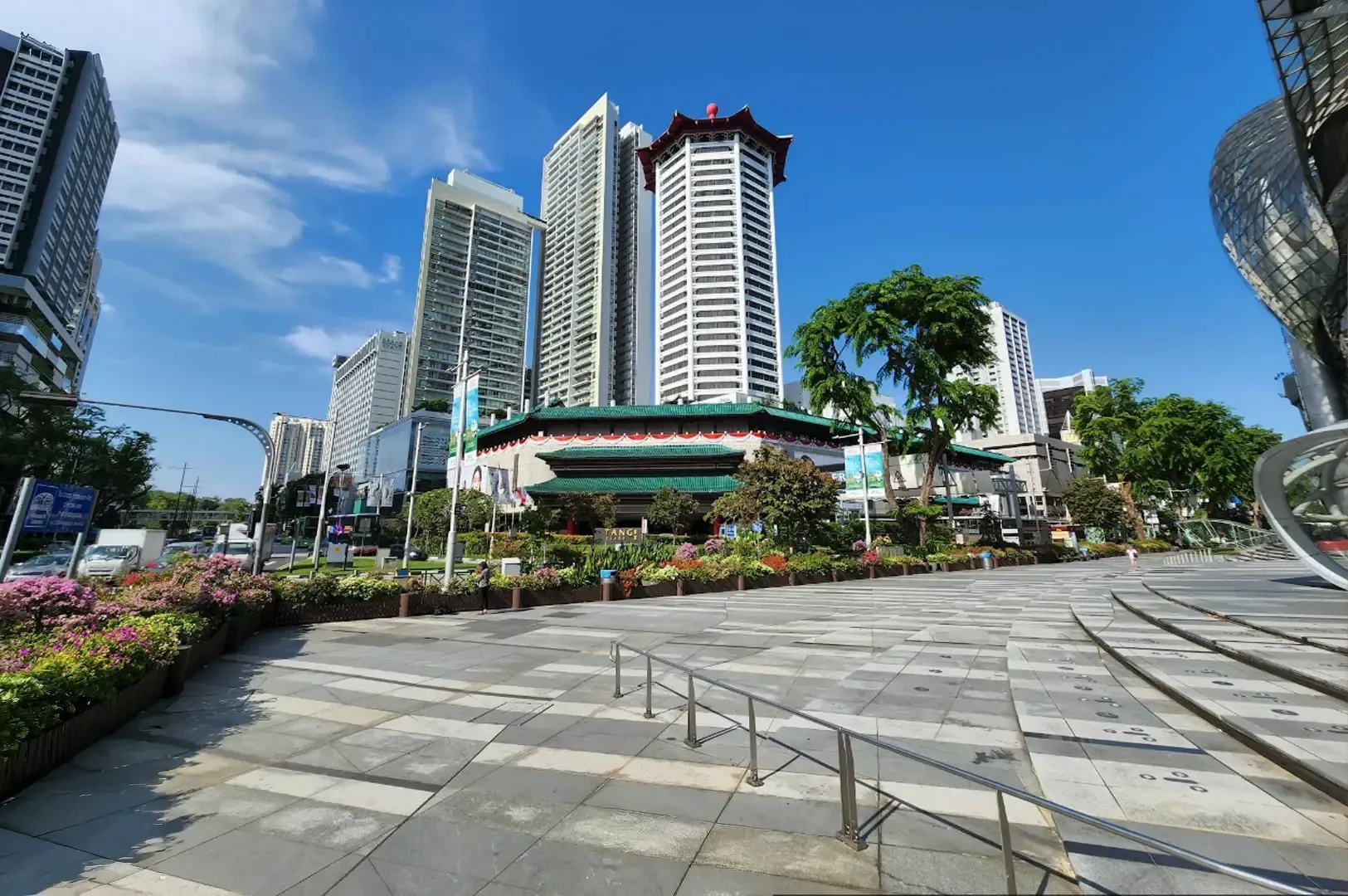 Sunny city plaza with high-rise buildings, flower beds, and a wide stone walkway