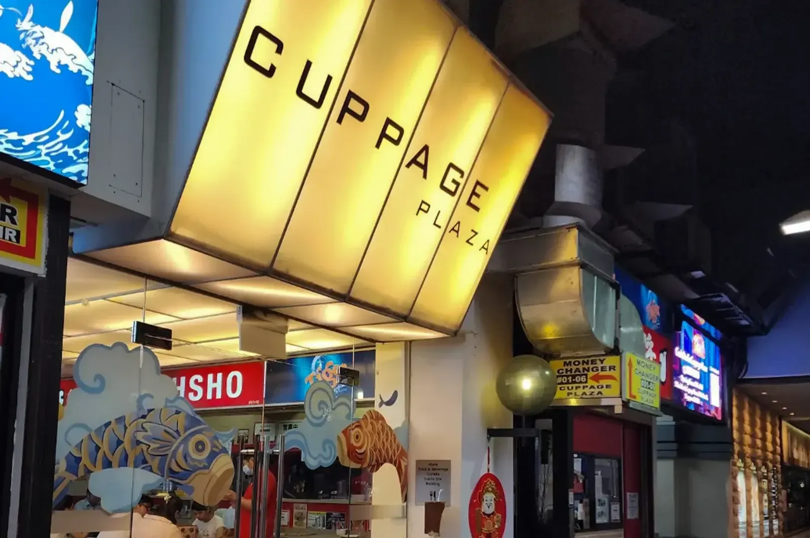 Illuminated Cuppage Plaza sign above a colorful indoor mall corridor with storefronts and neon signs