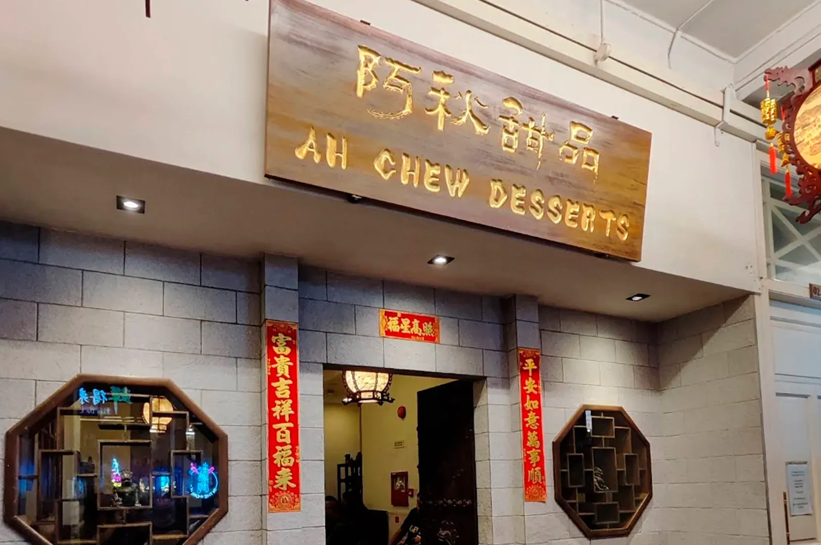 An Ah Chew Desserts shop entrance with a wooden sign, brick walls, traditional lanterns, and decorative red banners.