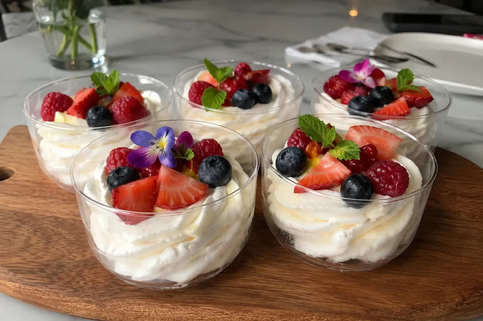 Lemon dessert cups topped with whipped cream and zest on a wooden table, with fresh lemons nearby