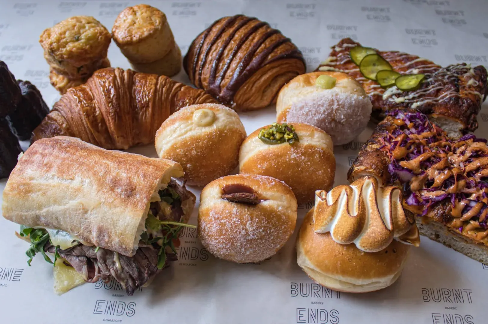 Assorted pastries and donuts displayed on parchment paper, including croissants, rolls, and filled buns.