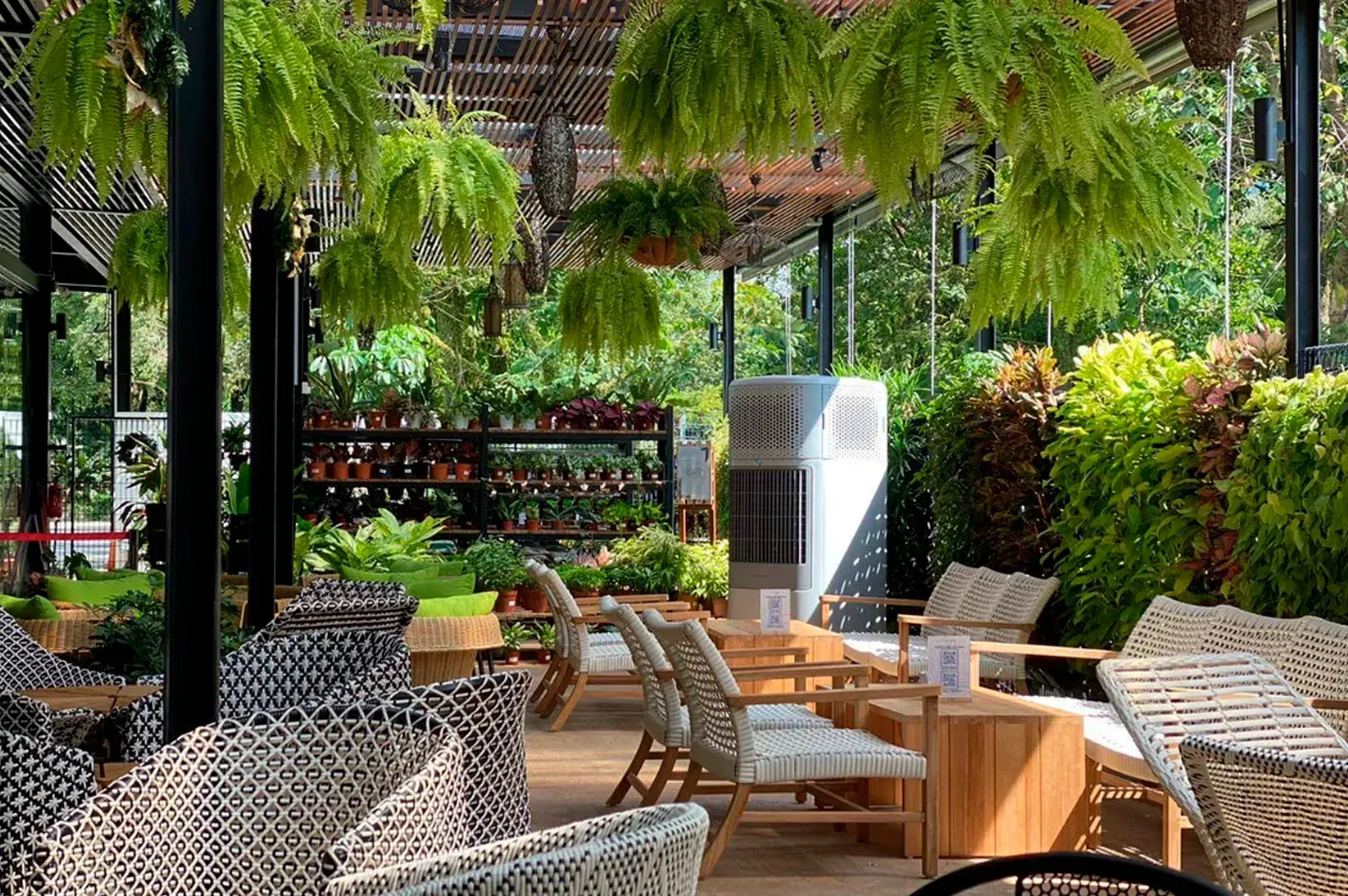 Outdoor patio with wicker chairs, wooden tables, and lush hanging greenery around a fountain