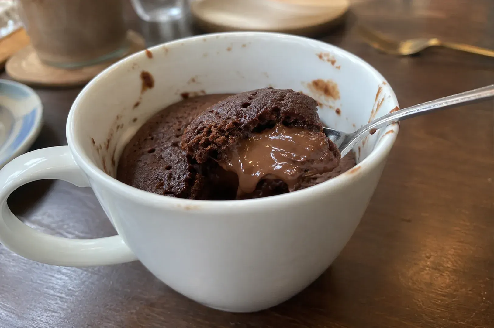 White cup of chocolate dessert with spoon on a wooden table, topped with cocoa powder