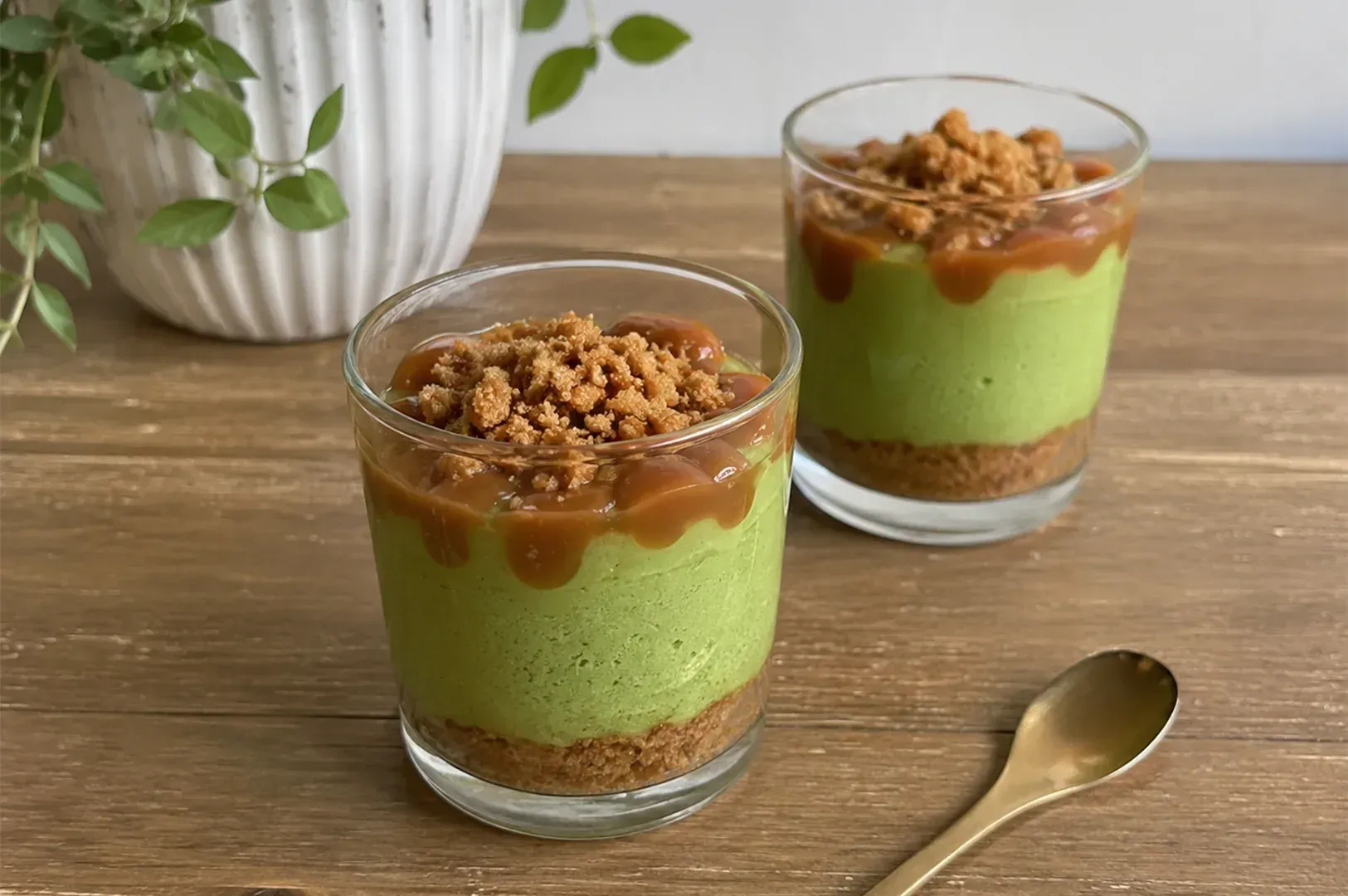 Two green dessert cups topped with caramel sauce and crumbled nuts on a wooden table
