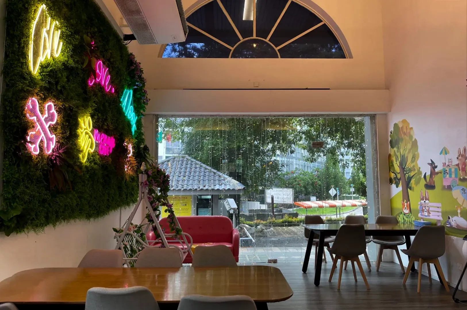 Cozy café interior with neon wall art, wooden tables, and large windows opening to a garden patio.