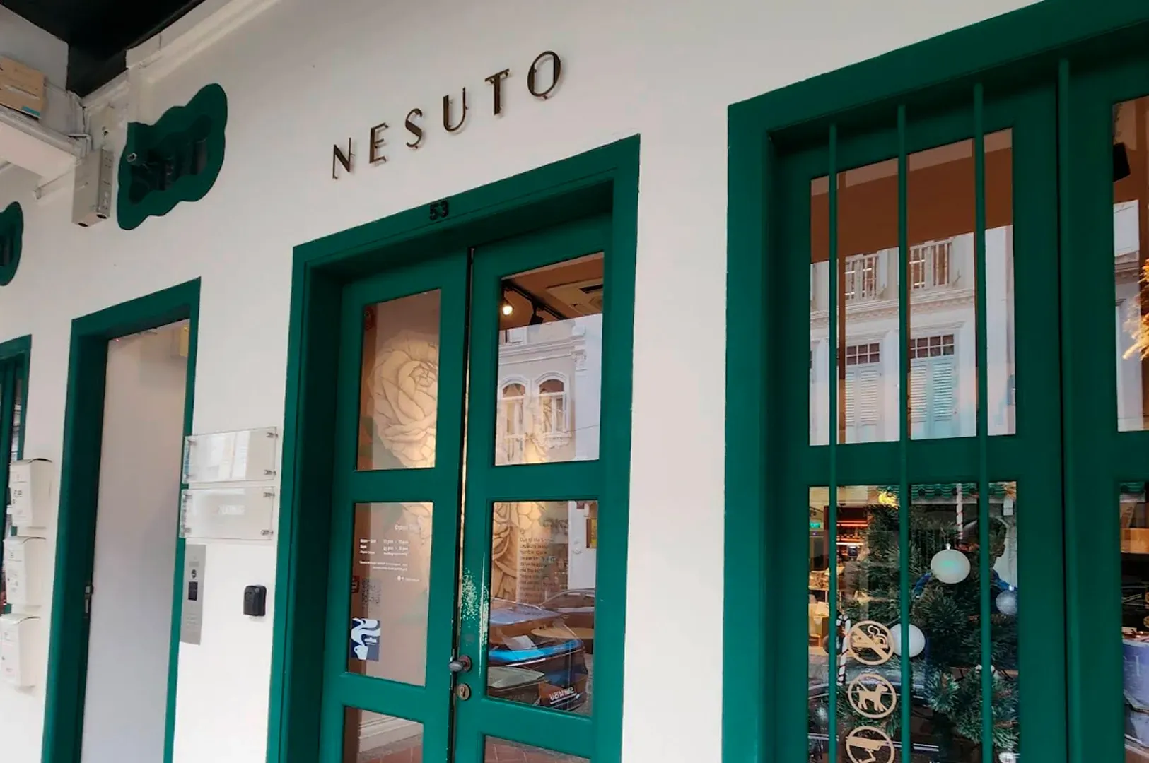 The storefront of Nesuto, featuring white walls, deep green window and door frames, and a glass-paneled entrance.