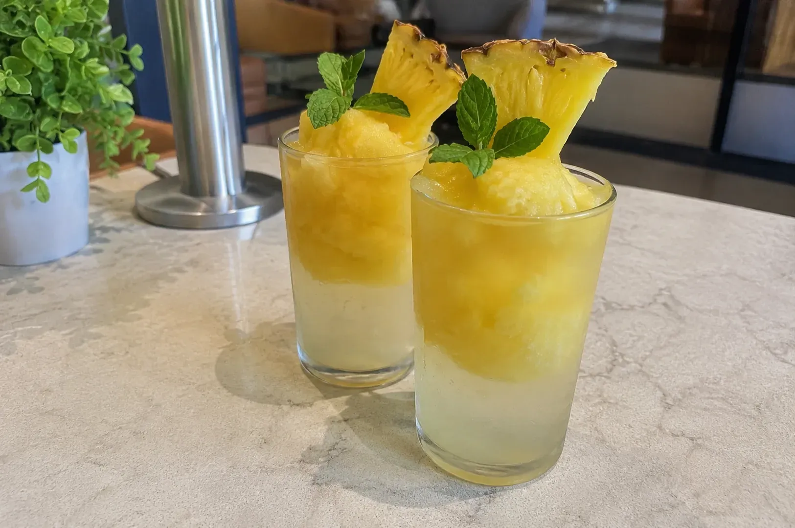 Two pineapple drinks with mint on a light stone table in a café