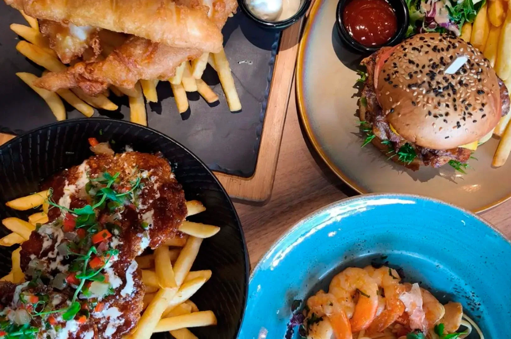 Assorted burgers and loaded fries on a table, with bowls of sauced food and ketchup sides