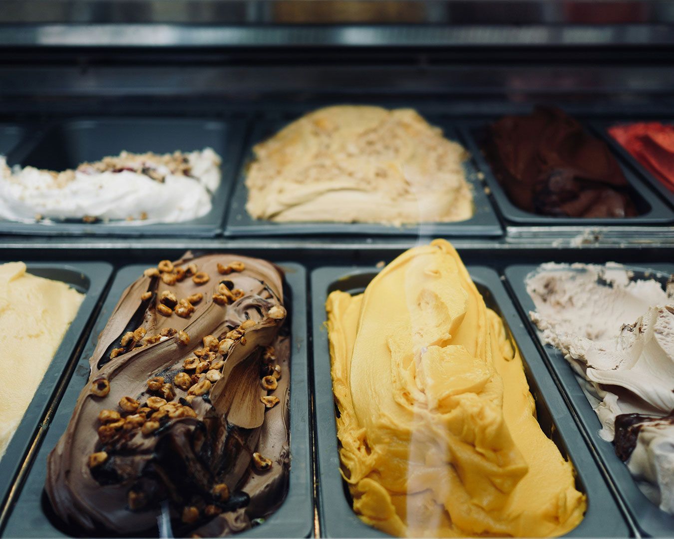 Assorted scoops of gelato in various flavours, displayed in a chilled tray with smooth textures and vibrant pastel colours.