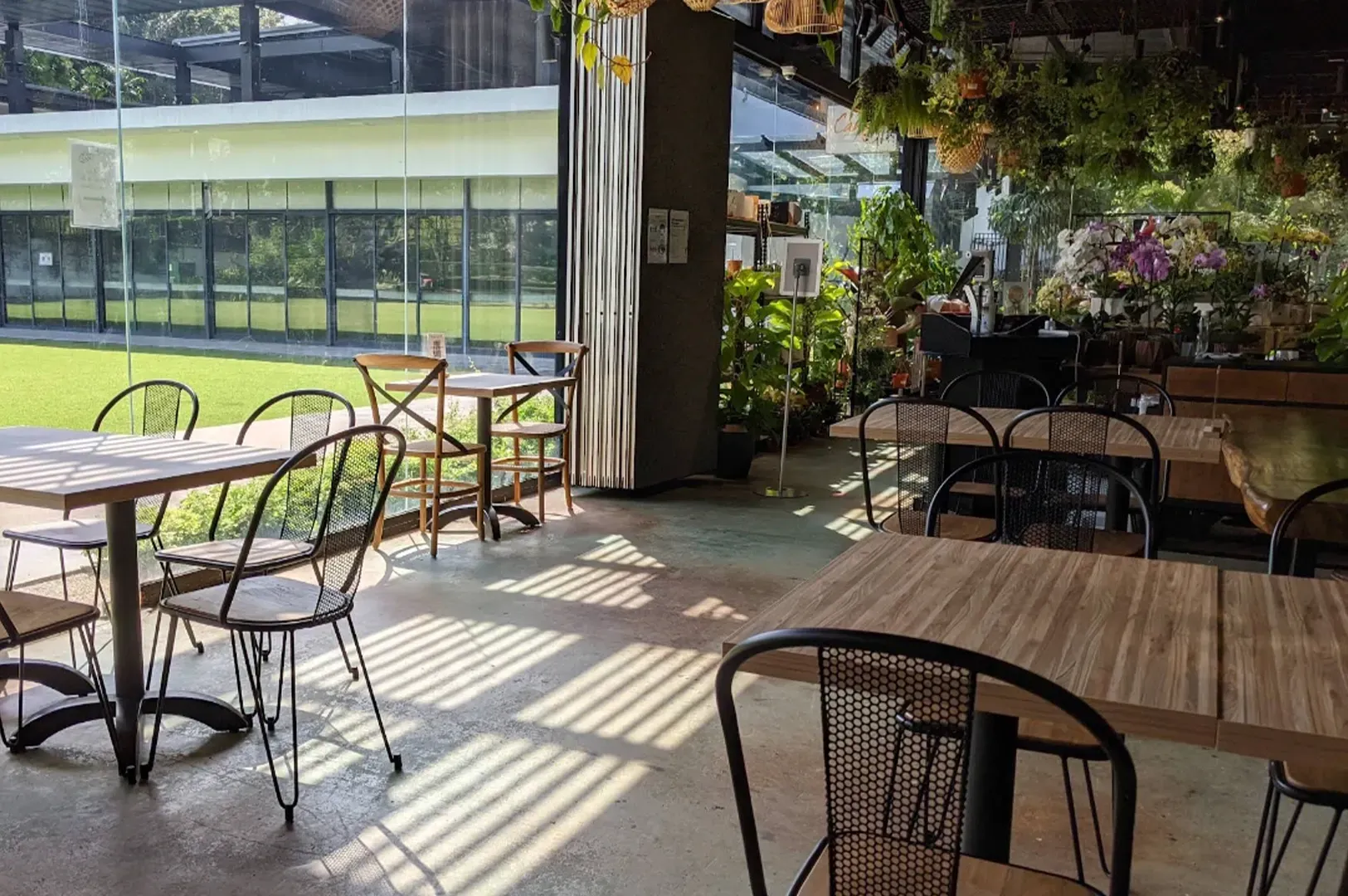 Sunlit café patio with metal chairs, tables, hanging plants, and long window shadows