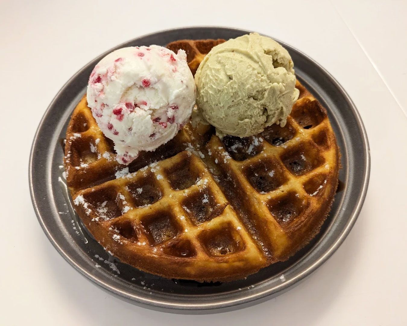 A crispy golden waffle topped with a generous scoop of ice cream, drizzled with sauce and served as a freshly prepared dessert.