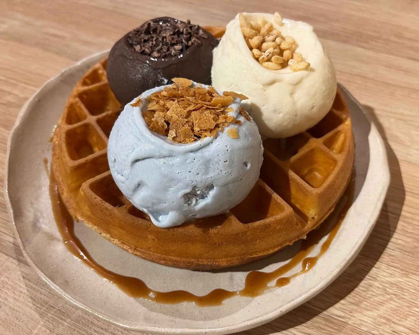 A warm, crispy waffle topped with a scoop of creamy vanilla ice cream, finished with syrup and light garnish on a white plate.