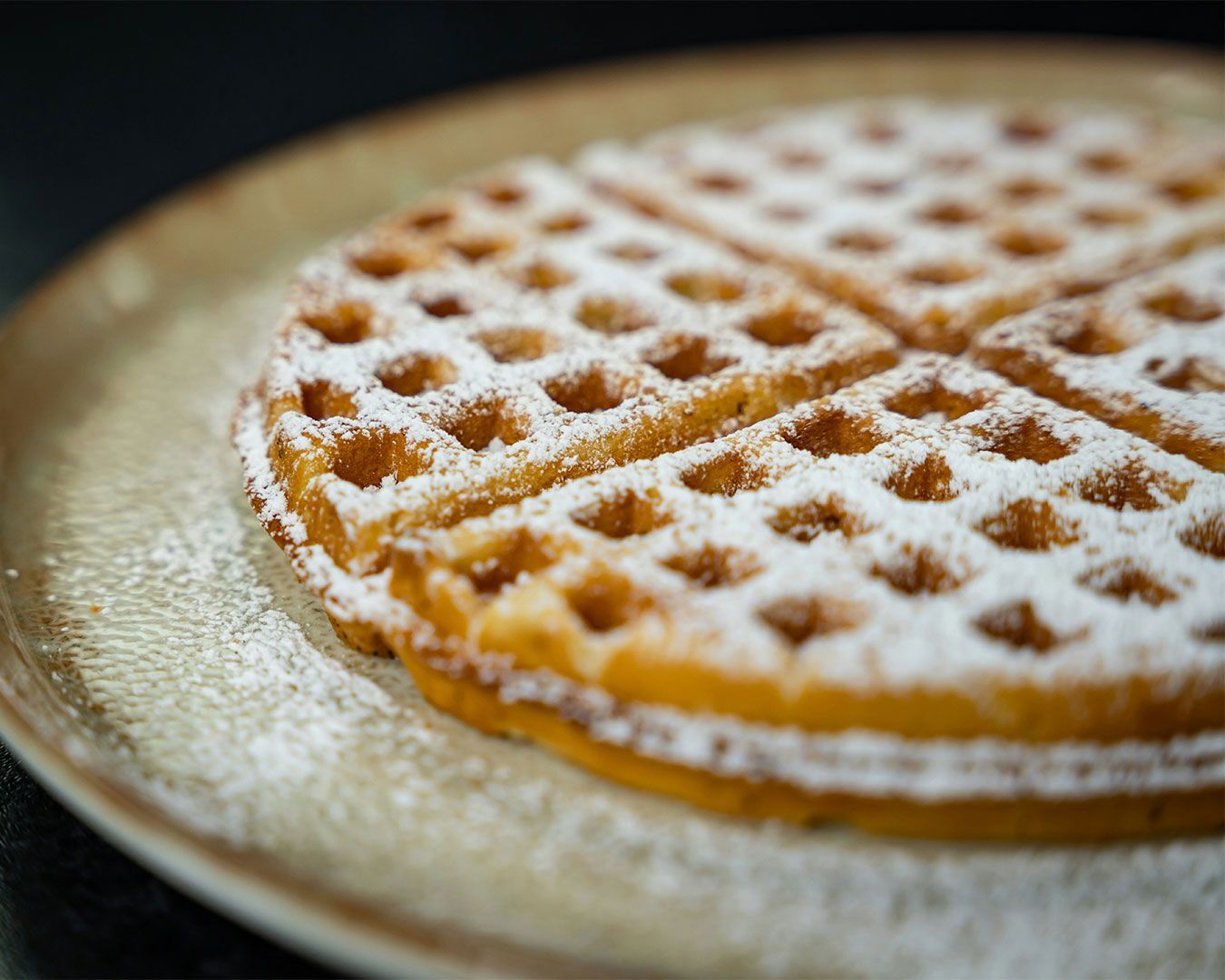 A freshly made waffle dusted with icing sugar, showing crisp edges and soft centre, served simply on a dessert plate.