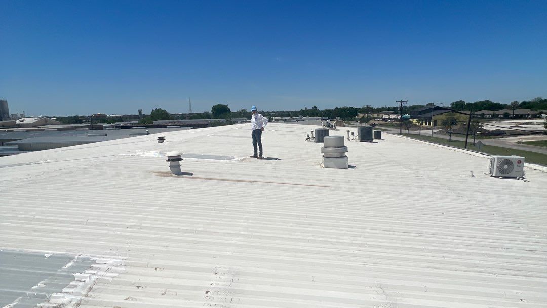 Man on white commercial roof under a blue sky.