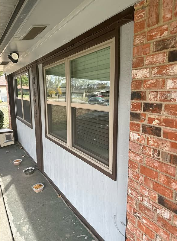A building's exterior with a window, brick wall, and light blue siding.