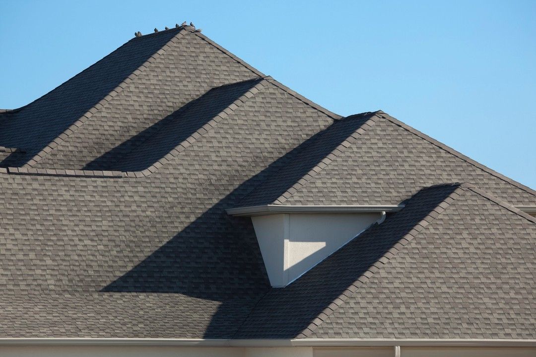 Gray shingled roof with a small, triangular architectural feature, against a clear blue sky.