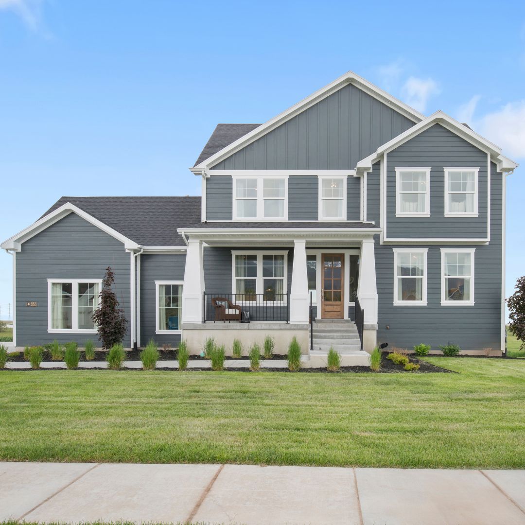 Two-story blue house with white trim, porch, and a well-kept lawn under a blue sky.