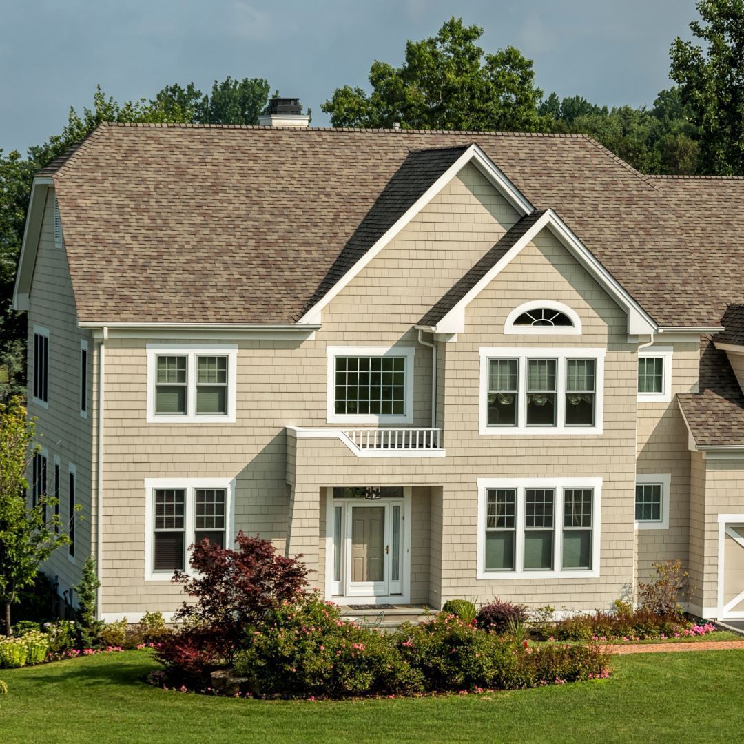 Tan two-story house with white trim, light brown roof, and lush green lawn.