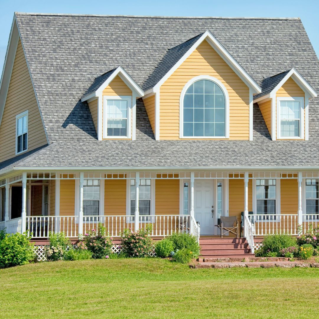 Yellow house with gray roof, white porch, and green lawn.