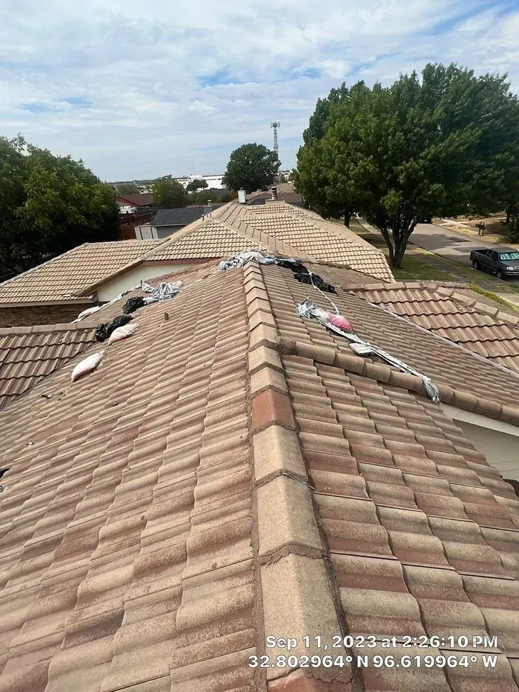 View of a tile roof with various materials on it under a cloudy sky.