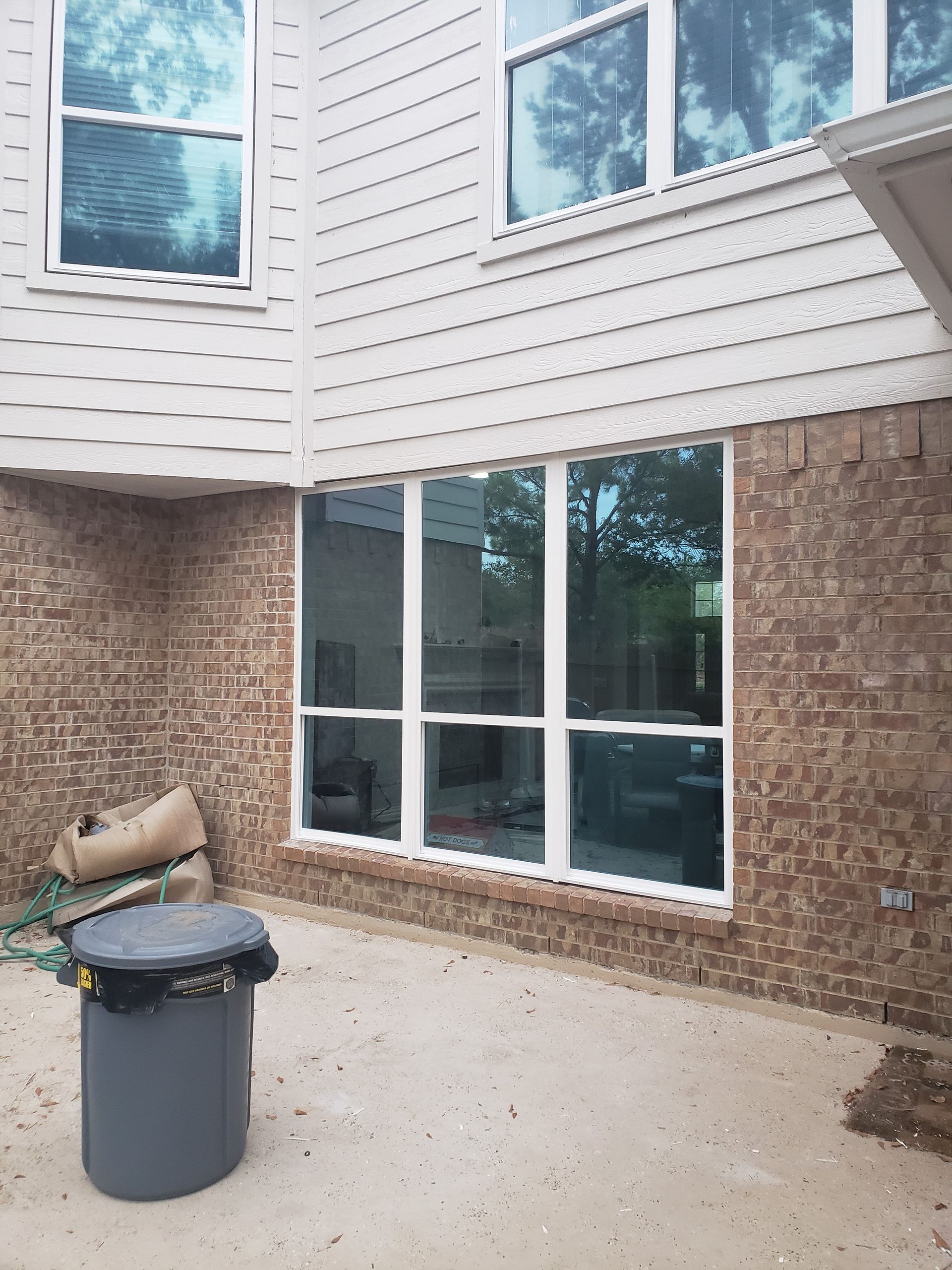 Exterior view of a house with brick and siding, large windows, and a trash can.