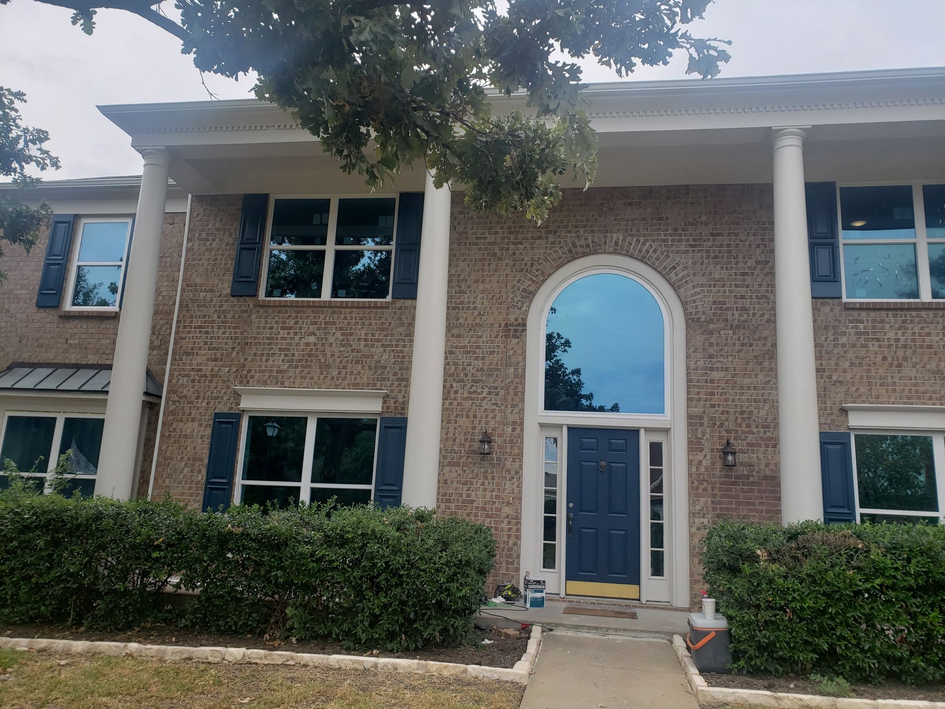 Two-story brick house with columns, dark blue shutters and door, and large windows with blue tints.