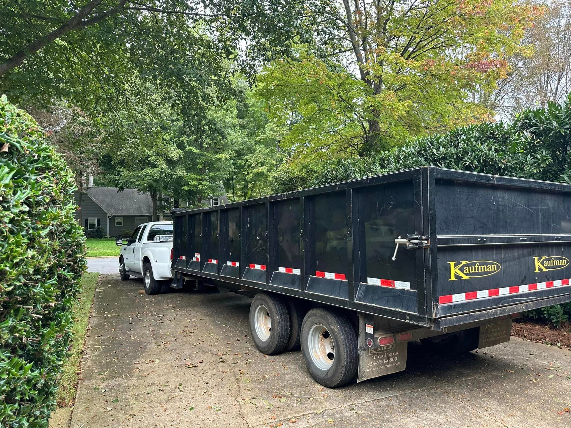 A dump truck is parked in a driveway next to a white truck.