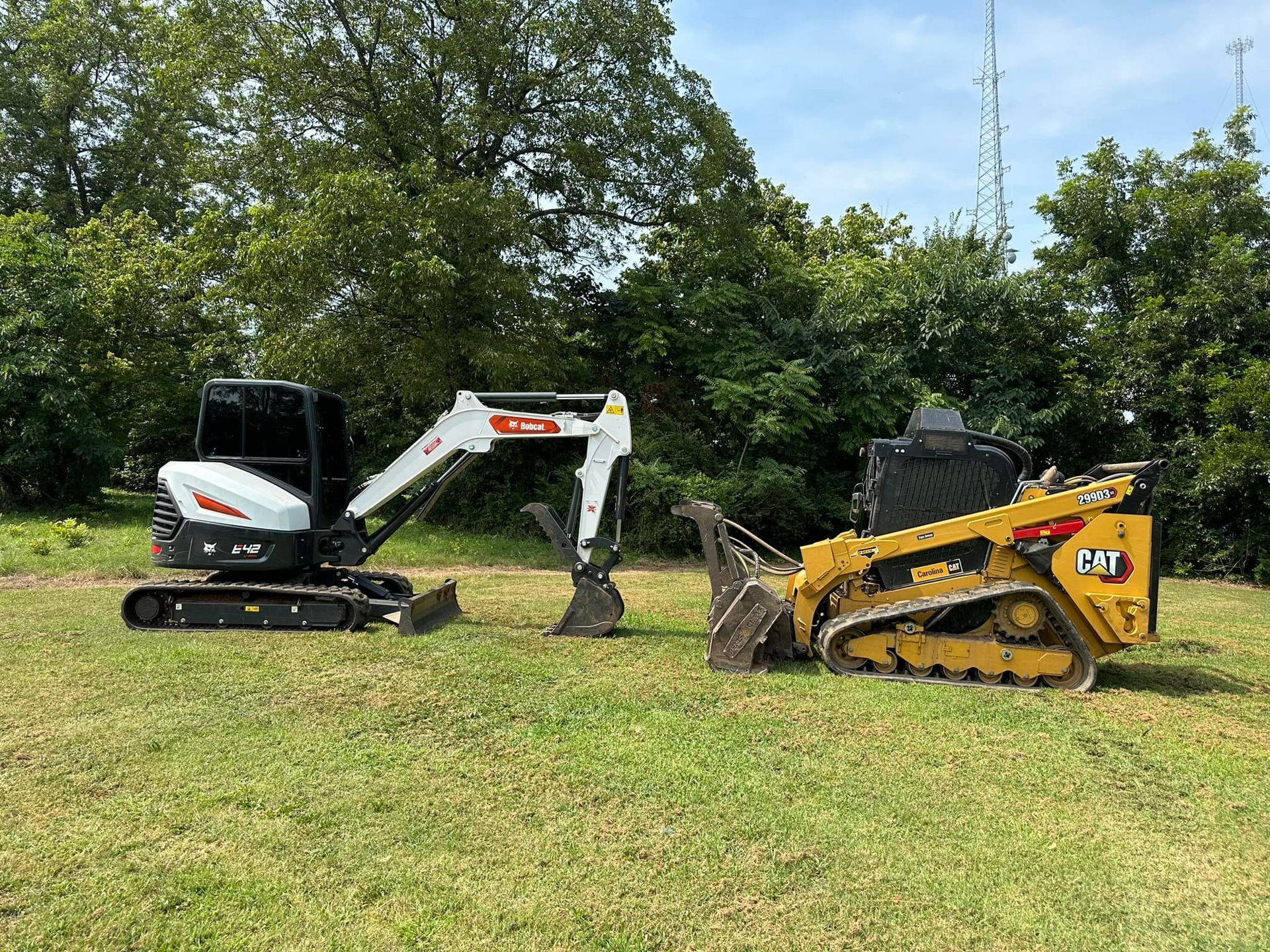 A small excavator and a bulldozer are parked in a grassy field.